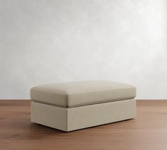 a beige ottoman sitting on top of a wooden floor next to a white wall in an empty room