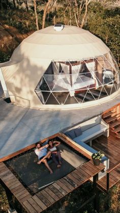 two people sitting on the roof of a yurt in the middle of some trees