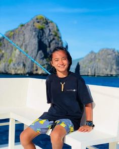 a young boy sitting on top of a white bench next to the ocean in front of an island