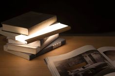 a stack of books sitting on top of a wooden table next to an open book