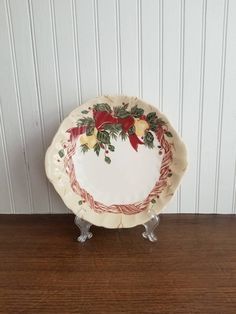 a white plate with red bows and holly on it sitting on a wooden table next to a wall