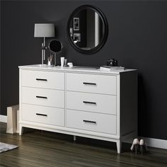 a white dresser sitting in front of a black wall with a round mirror above it