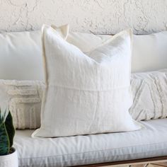 a white pillow sitting on top of a couch next to a potted plant