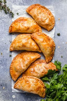 four empanada pastries on a piece of parchment paper with parsley next to them