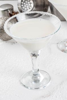 two glasses filled with white liquid sitting on top of a table next to silver ornaments