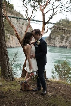 a man and woman standing next to each other in front of trees near the water