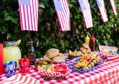 a table topped with plates of food next to american flags hanging from the side of trees