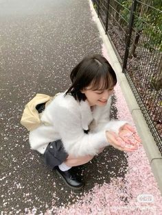 a woman kneeling down on the ground with her hands in front of her face and pink flowers all around her