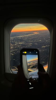 a person holding up a cell phone in front of an airplane window with the sun setting