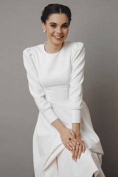 a woman sitting on top of a chair wearing a white dress and smiling at the camera