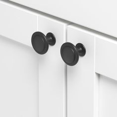 two black knobs on the front of a white kitchen cabinet with handles and pulls