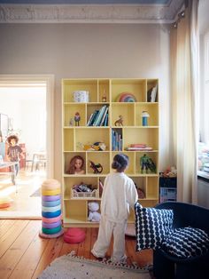 two children are standing in front of a bookshelf with toys on the floor