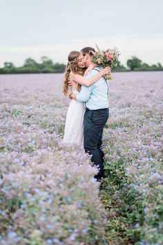 a man and woman are standing in a field with flowers on their heads, hugging