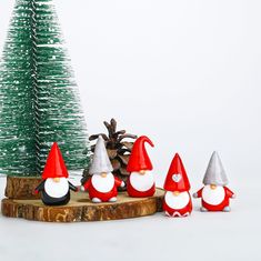 a group of gnome figurines sitting next to a small christmas tree and pine cone