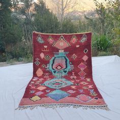 an old rug is sitting on a table outside in the sun with trees and bushes behind it