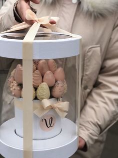 a person holding a white box with chocolates in it and a bow on the top