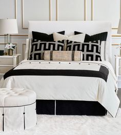 a white bed topped with black and white pillows next to a night stand filled with lamps