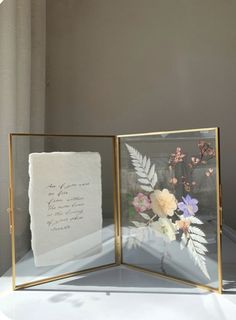 two framed pictures with flowers on them sitting on top of a white tablecloth covered table