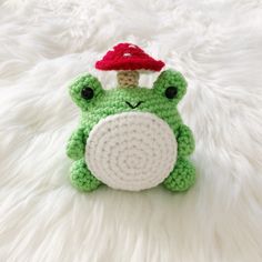 a crocheted frog with a red mushroom on its head sitting on a white rug