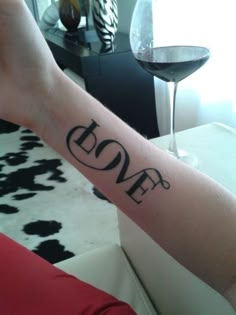 a woman's arm with the word love on it and a wine glass next to her