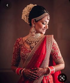 a woman in a red and gold bridal outfit with her hands on her hips