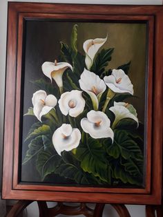 an oil painting of white flowers in a wooden frame on a table next to a wall