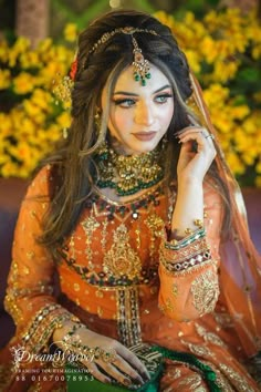 a woman in an orange and gold outfit sitting on a couch with flowers behind her