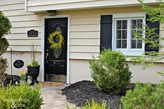 a black door with a wreath on the side of it and some plants in front