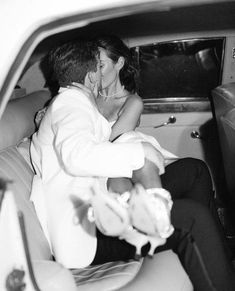 a man and woman sitting in the back of a car, one kissing while the other is