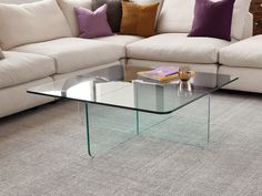 a glass coffee table sitting on top of a carpeted floor next to a couch