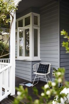 a white chair sitting on top of a wooden porch next to a tree and bushes