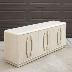 a white cabinet sitting on top of a cement floor next to a garage door with two doors