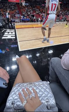 a woman sitting on top of a basketball court next to a man holding a white purse