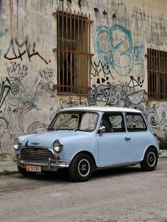 an old blue and white mini car parked in front of a wall with graffiti on it