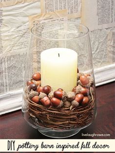 an image of a candle in a glass vase with acorns and pine cones