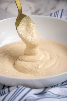 a spoon full of cream being held over a bowl with some kind of sauce in it