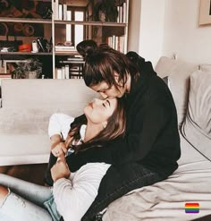 two young women sitting on top of a couch next to each other in front of a bookshelf