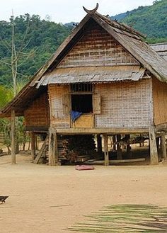 an old wooden house in the middle of a dirt field with mountains in the background