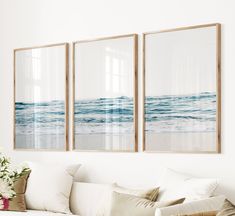 three framed pictures hang on the wall above a couch in a living room with white furniture