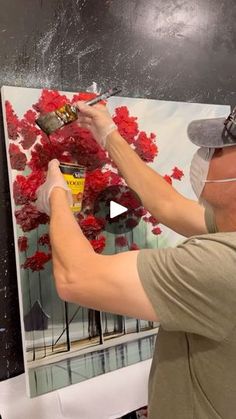 a man is painting red flowers on a canvas