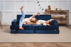 two children laying on a blue couch with their arms in the air and one child reaching up