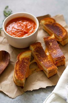 grilled cheese sandwiches with tomato sauce in a white bowl and spoon on a piece of parchment paper