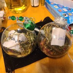 two glass ornaments with writing on them sitting on a table next to other christmas decorations