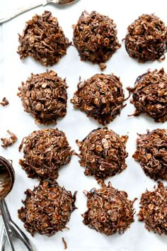 chocolate cookies and spoons are on a white surface with some oats in the middle