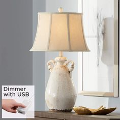 a lamp that is on top of a table next to a hand holding a remote control