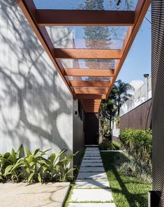 an outdoor walkway leading to a house with wood and glass on the roof, surrounded by greenery