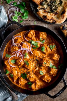 a skillet filled with chicken tikka and onions on top of a wooden table