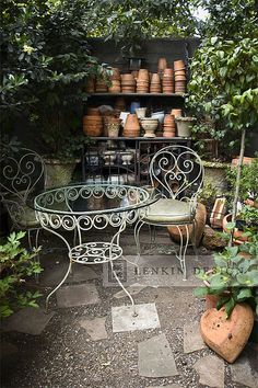 an outdoor table and chairs with pots on the shelves behind them in a garden setting