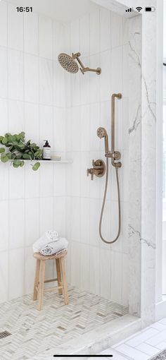 a white tiled bathroom with a wooden stool and shower head