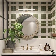 a bathroom with green and white tiles on the walls, a round mirror above the sink